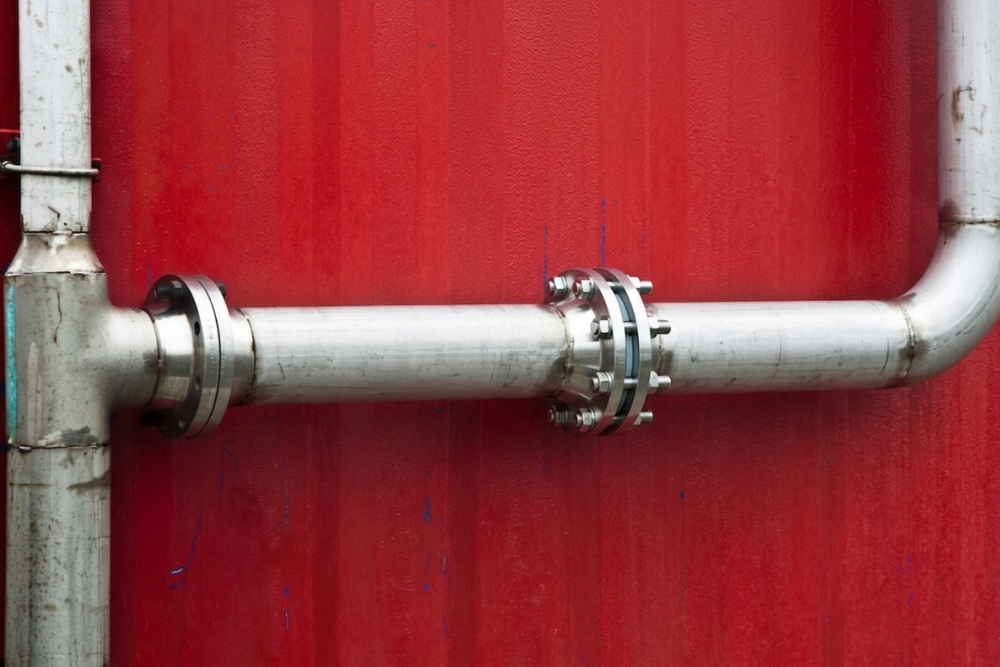 The same stainless steel pipe flange joint now dry and fully sealed with a bolted repair collar in place, photographed after the burst pipe repair was completed and pressure tested against the same red wall background
