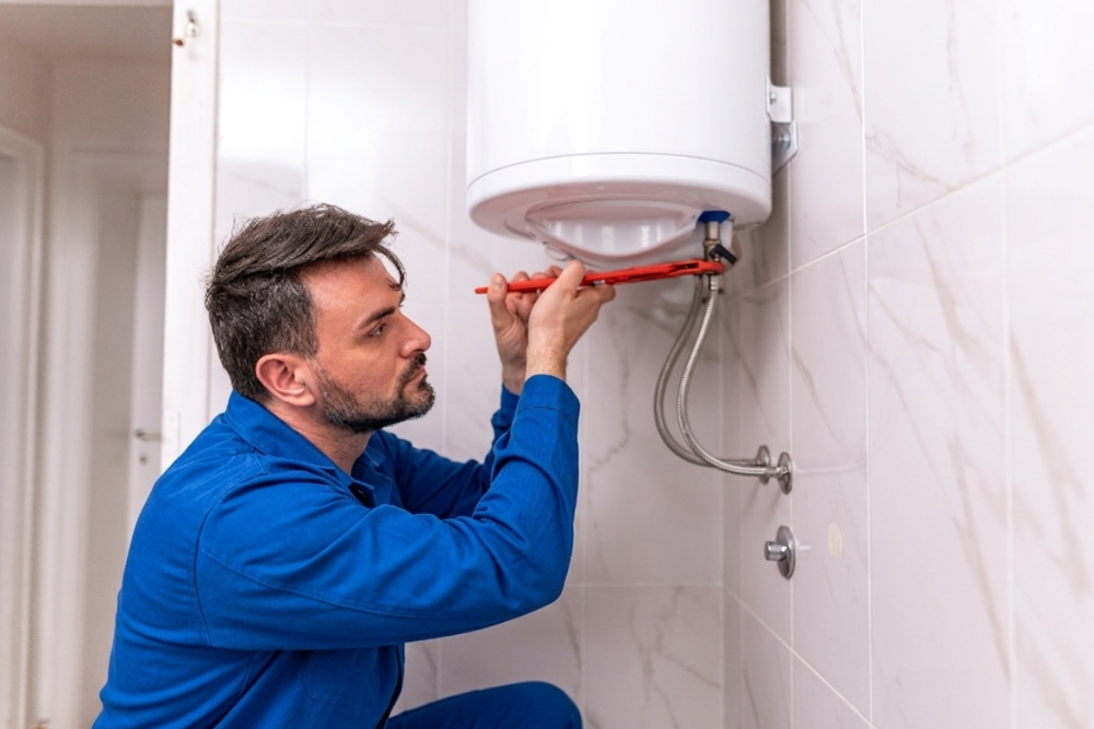 Quick Fix Dubai technician examining a clean, newly installed white water heater tank mounted on a marble-tiled bathroom wall, with a red spanner in hand checking the braided steel supply connection after completing a water heater repair