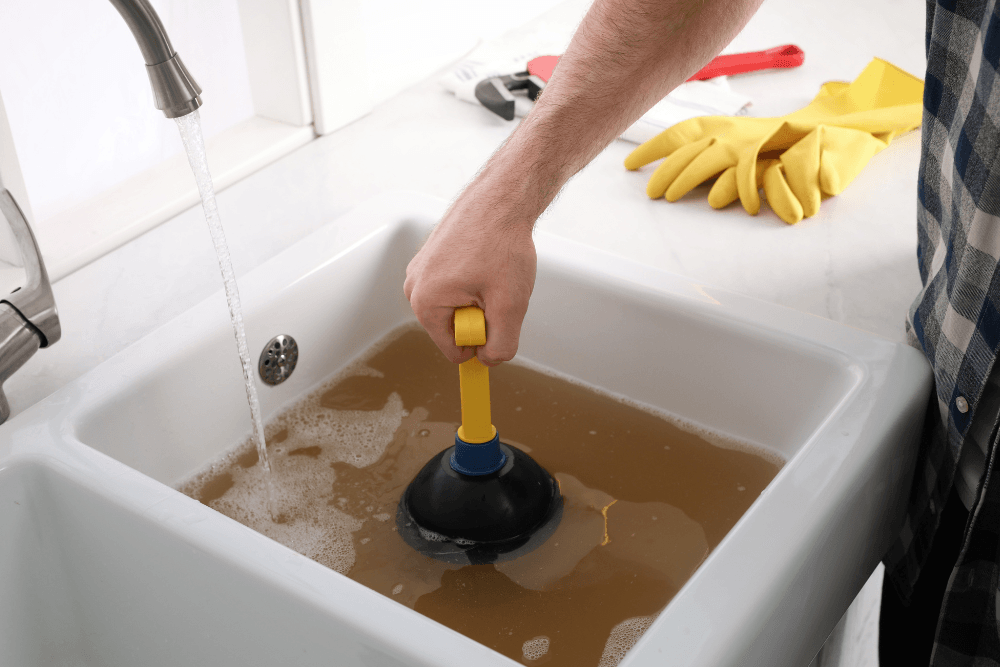 A kitchen sink and tap with a plunger being used to clear a blockage, representative of the everyday plumbing fixtures a new Dubai resident will encounter in their home