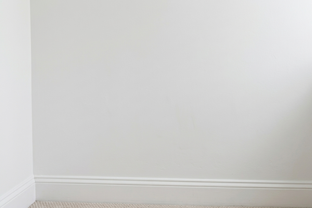 A fully repaired and repainted interior wall in plain white finish, photographed at the same corner where mould and water staining previously spread from an undetected pipe leak, showing the completed remediation result